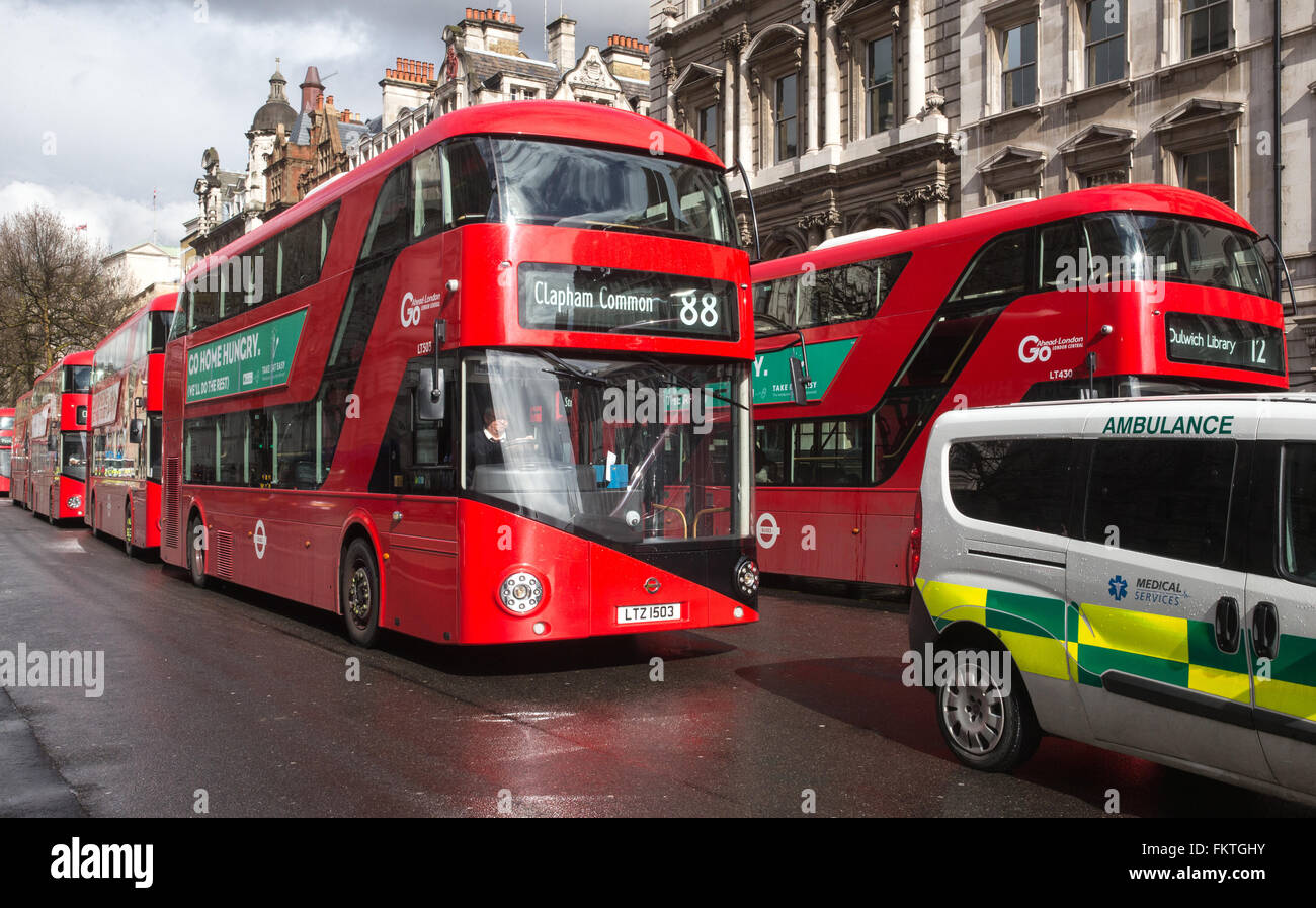 Iconico autobus rossi di Londra in Whitehall vicino al Parlamento con un ambulanza in primo piano Foto Stock