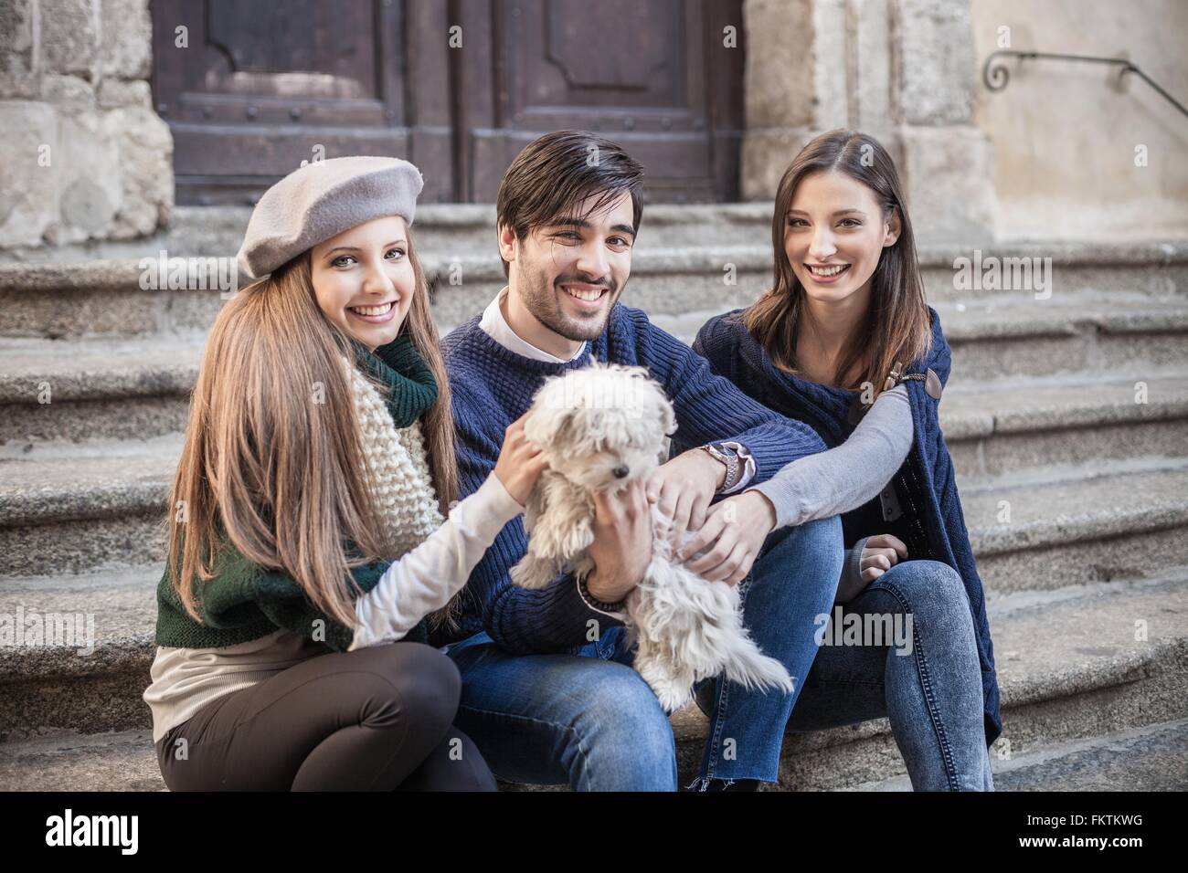 Amici seduti fianco a fianco su gradini holding fluffy cane guardando sorridente della fotocamera Foto Stock