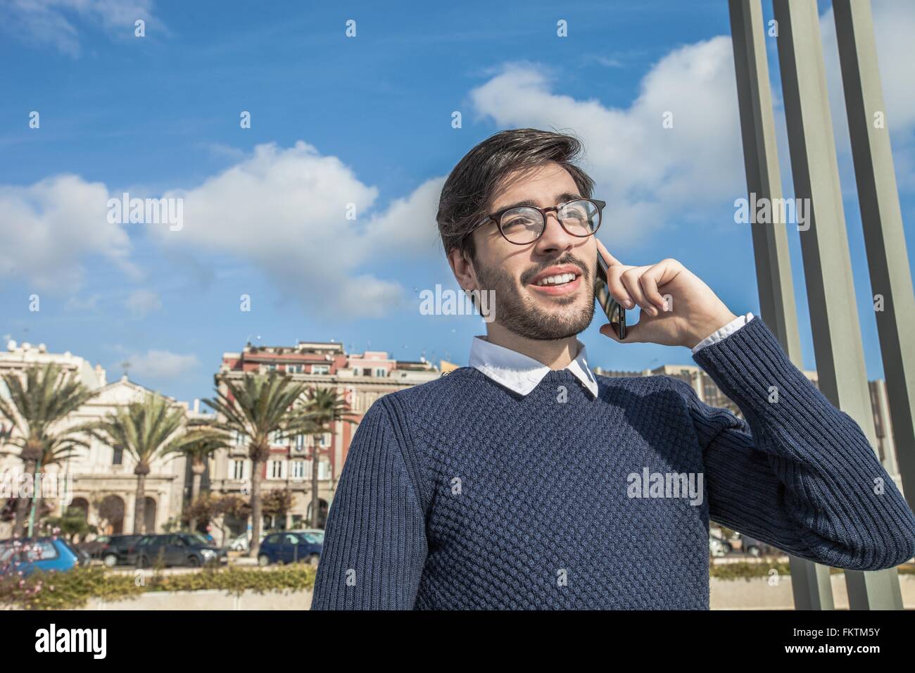 Giovane uomo che indossa occhiali utilizza lo smartphone che guarda lontano sorridente Foto Stock