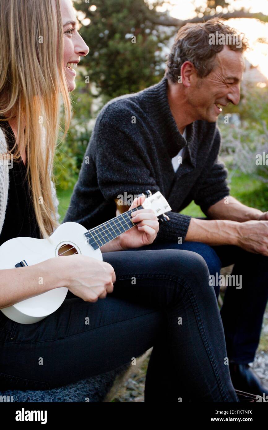 Giovane seduti insieme, donna giocando ukulele Foto Stock