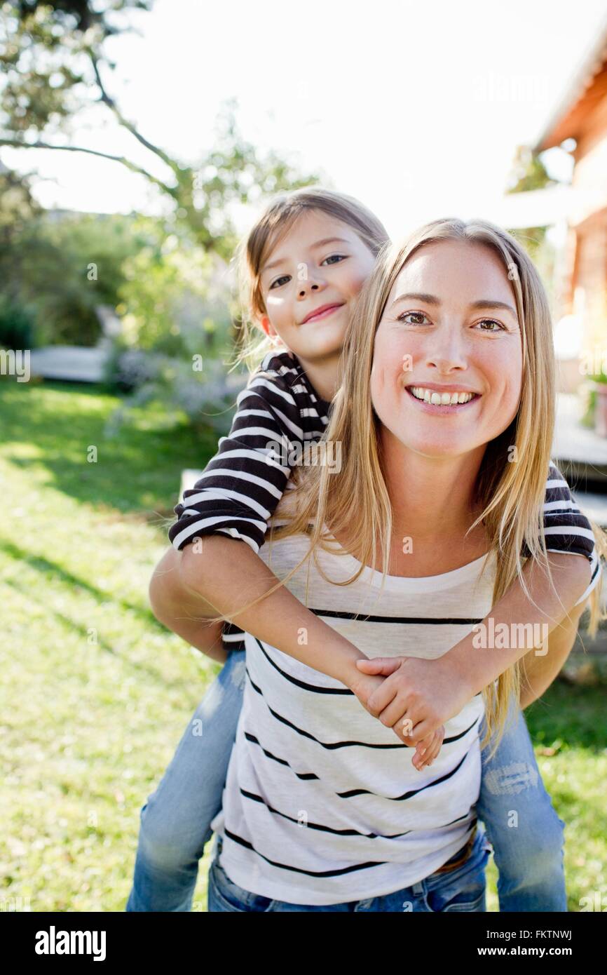 Madre dando figlia piggy back Foto Stock