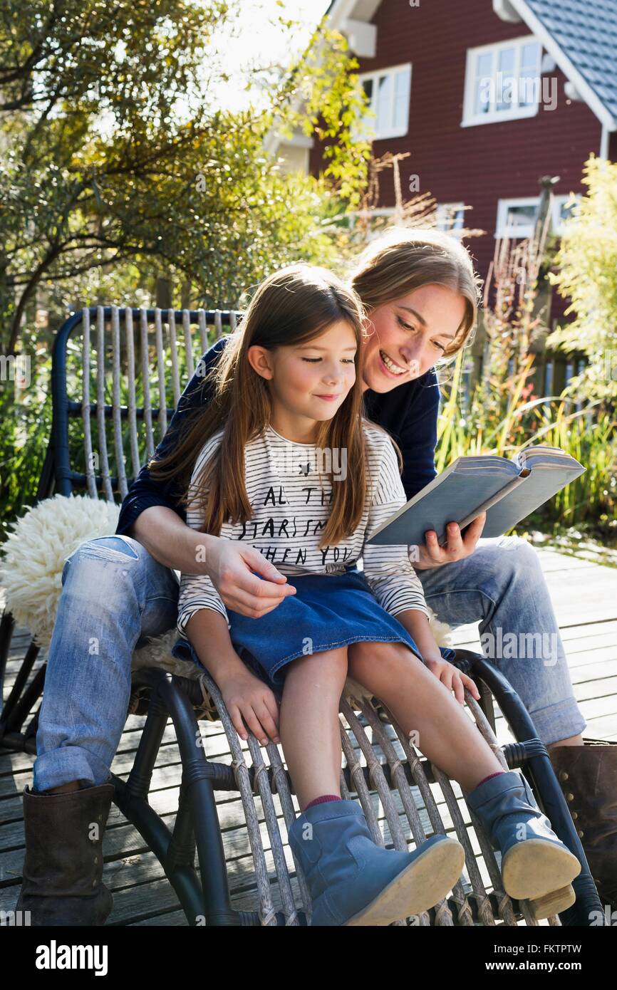 Madre e figlia seduti su una sedia all'aperto libro di lettura Foto Stock