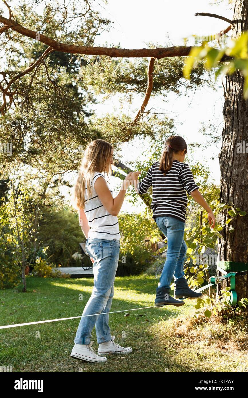 Bilanciamento figlia lungo la fune sull'albero, madre tenendo la mano Foto Stock