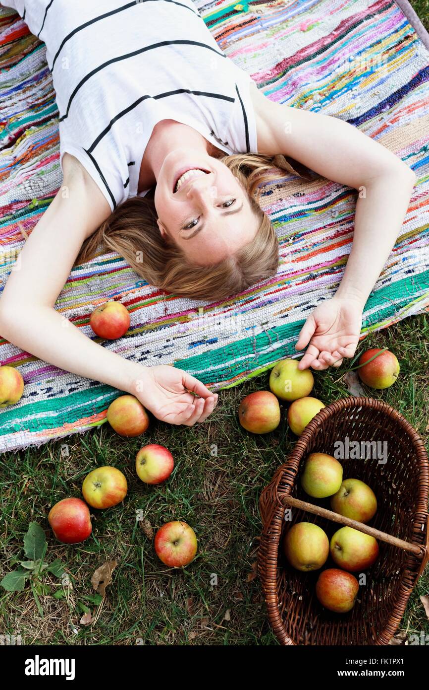 Donna sdraiata sul tappeto a strisce con cesto di mele Foto Stock