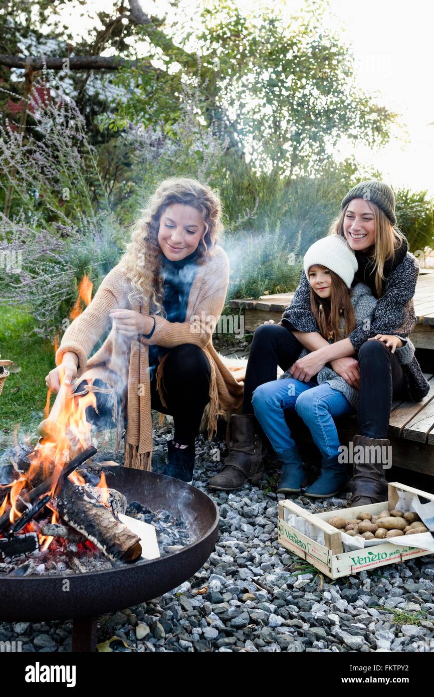 Due donne e ragazza seduta da una buca per il fuoco, rilassante Foto Stock