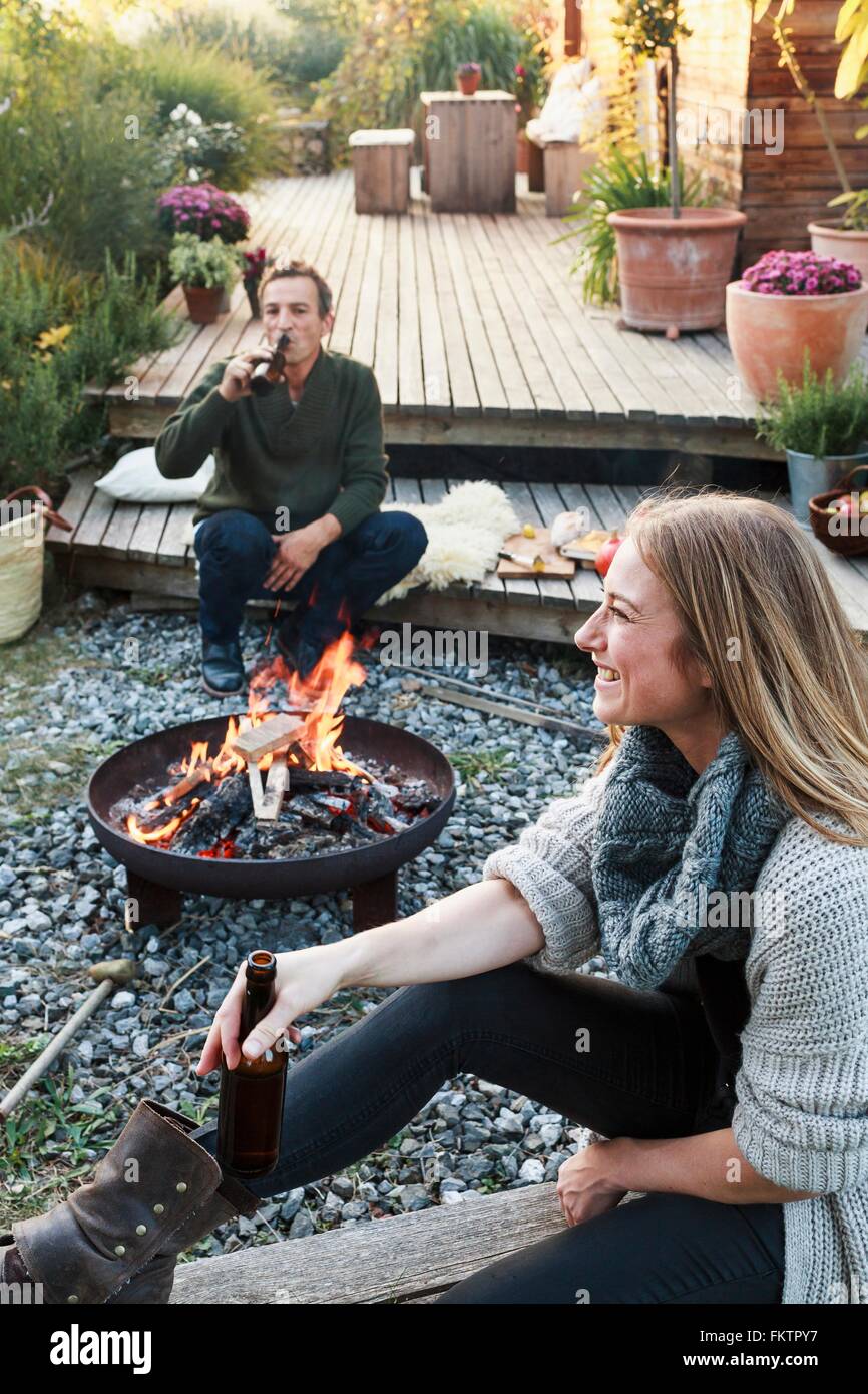 L uomo e la donna seduta da una buca per il fuoco con la birra, rilassante Foto Stock