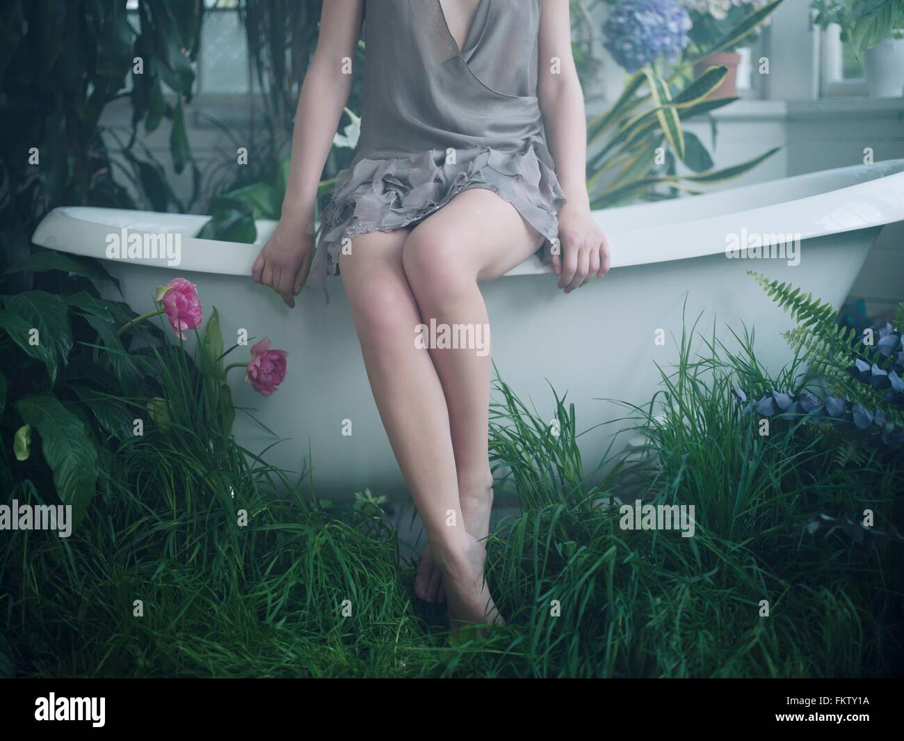 Giovane donna seduta sul bordo della vasca in bagno riempito con piante Foto Stock