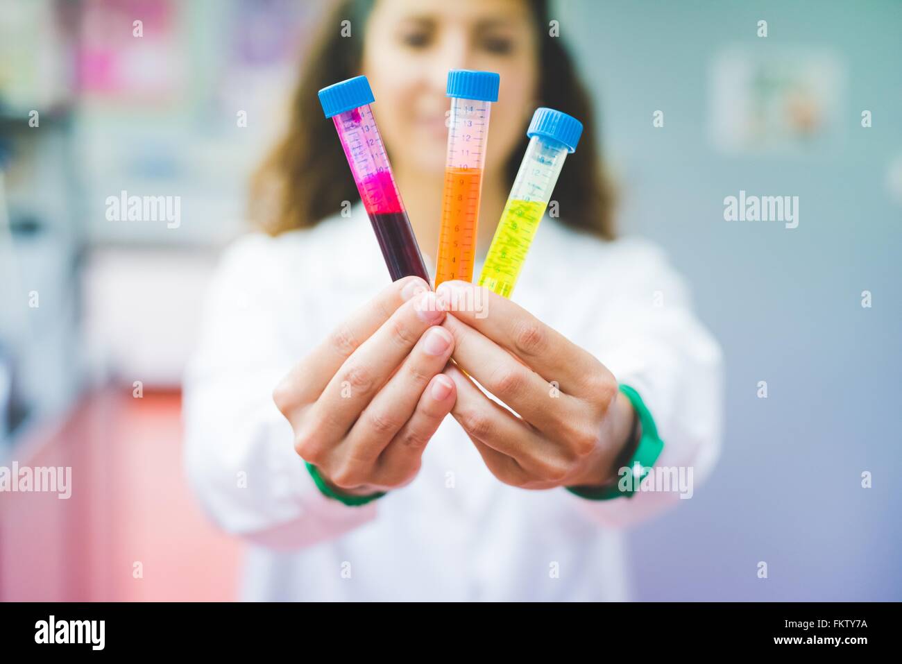 Donna scienziato holding soluzione di tre diversi coloranti fluorescenti Foto Stock
