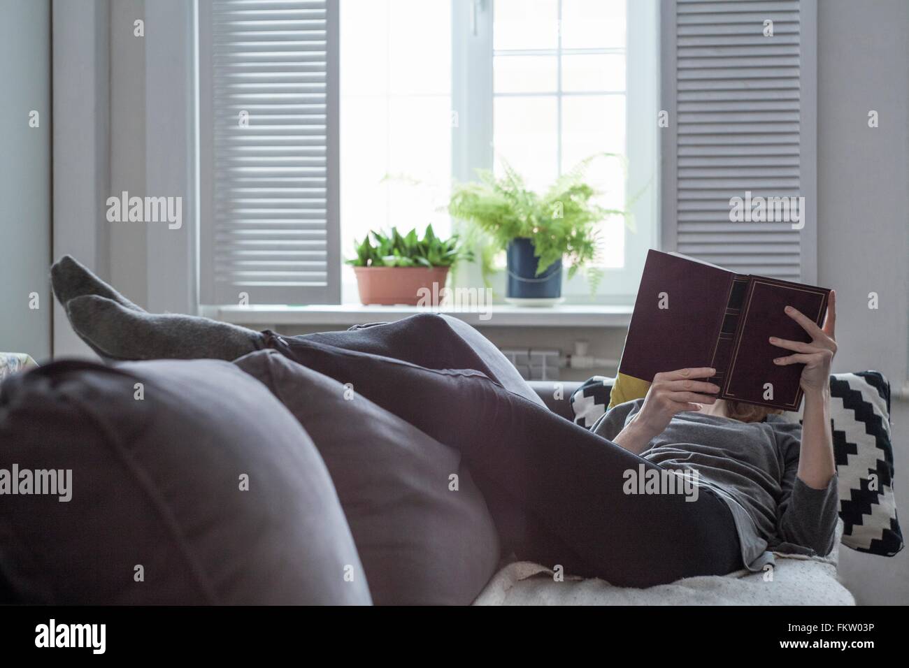 Donna sdraiata su divano la lettura di un libro Foto Stock