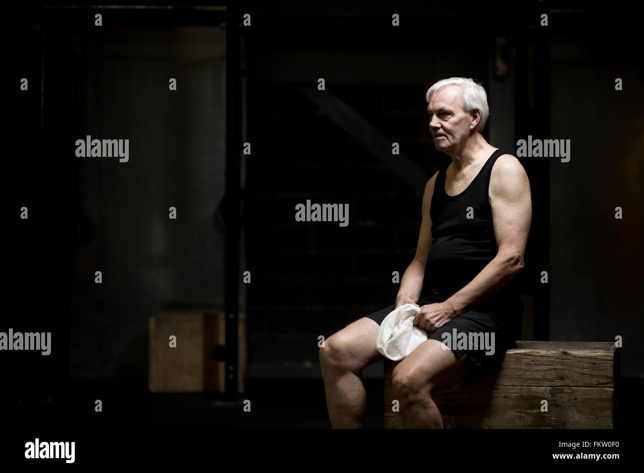 Senior uomo seduto appoggiato in palestra scuro Foto Stock