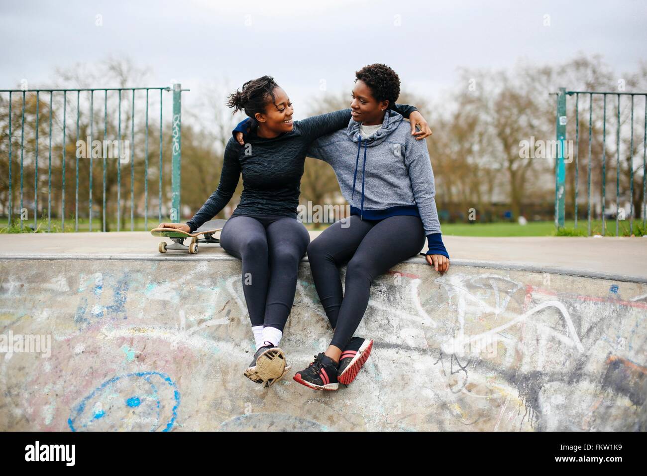 Due giovani donne lo skateboard amici in seduta skateboard park Foto Stock