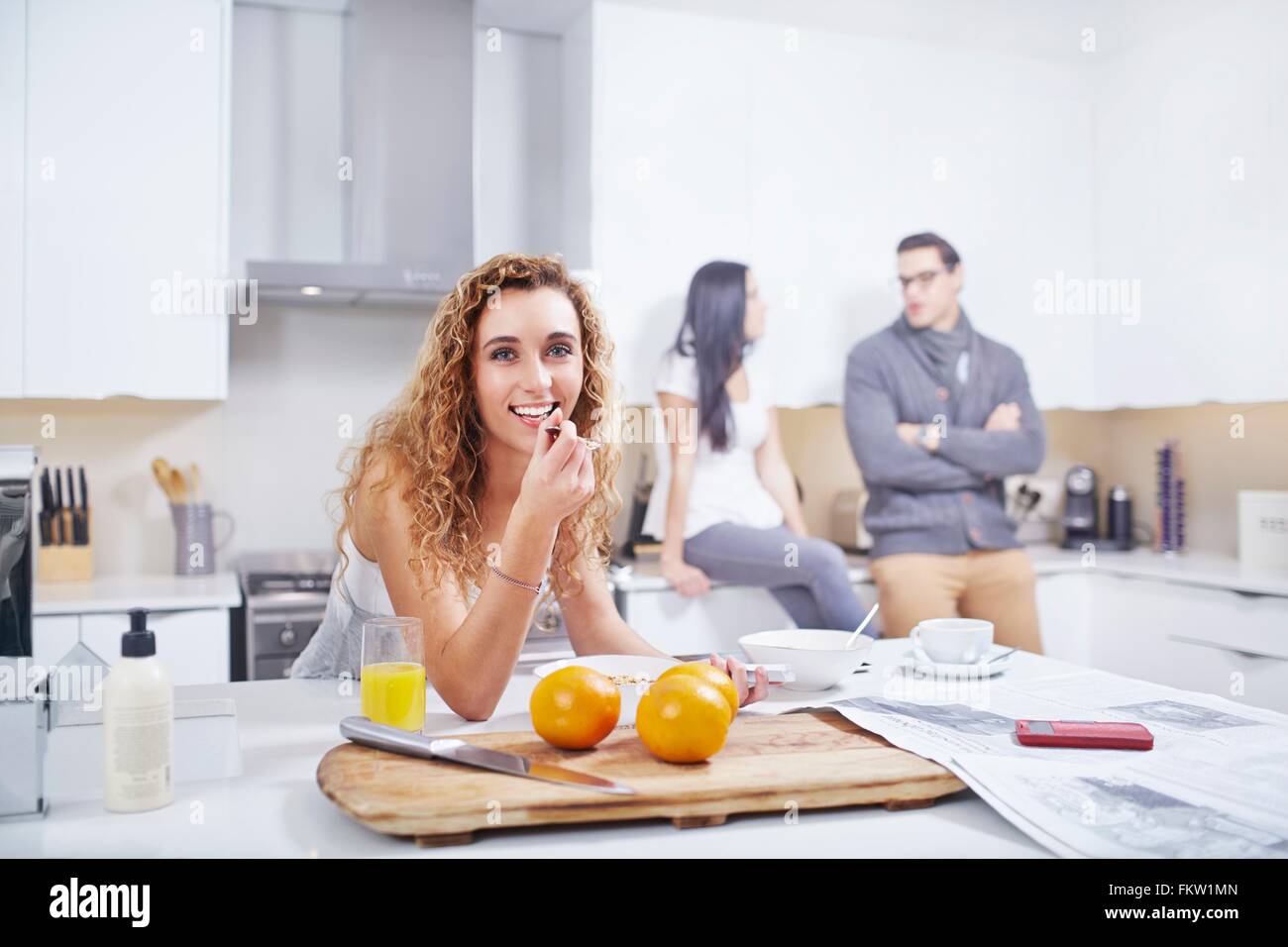 Ritratto di giovane donna di mangiare cereali per la colazione al banco di cucina Foto Stock