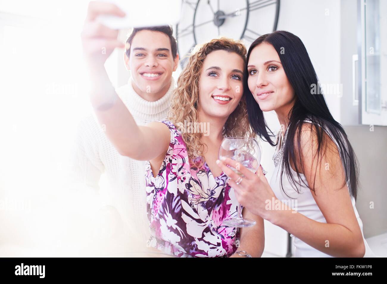 Tre giovani amici adulti in posa per smartphone selfie in cucina Foto Stock