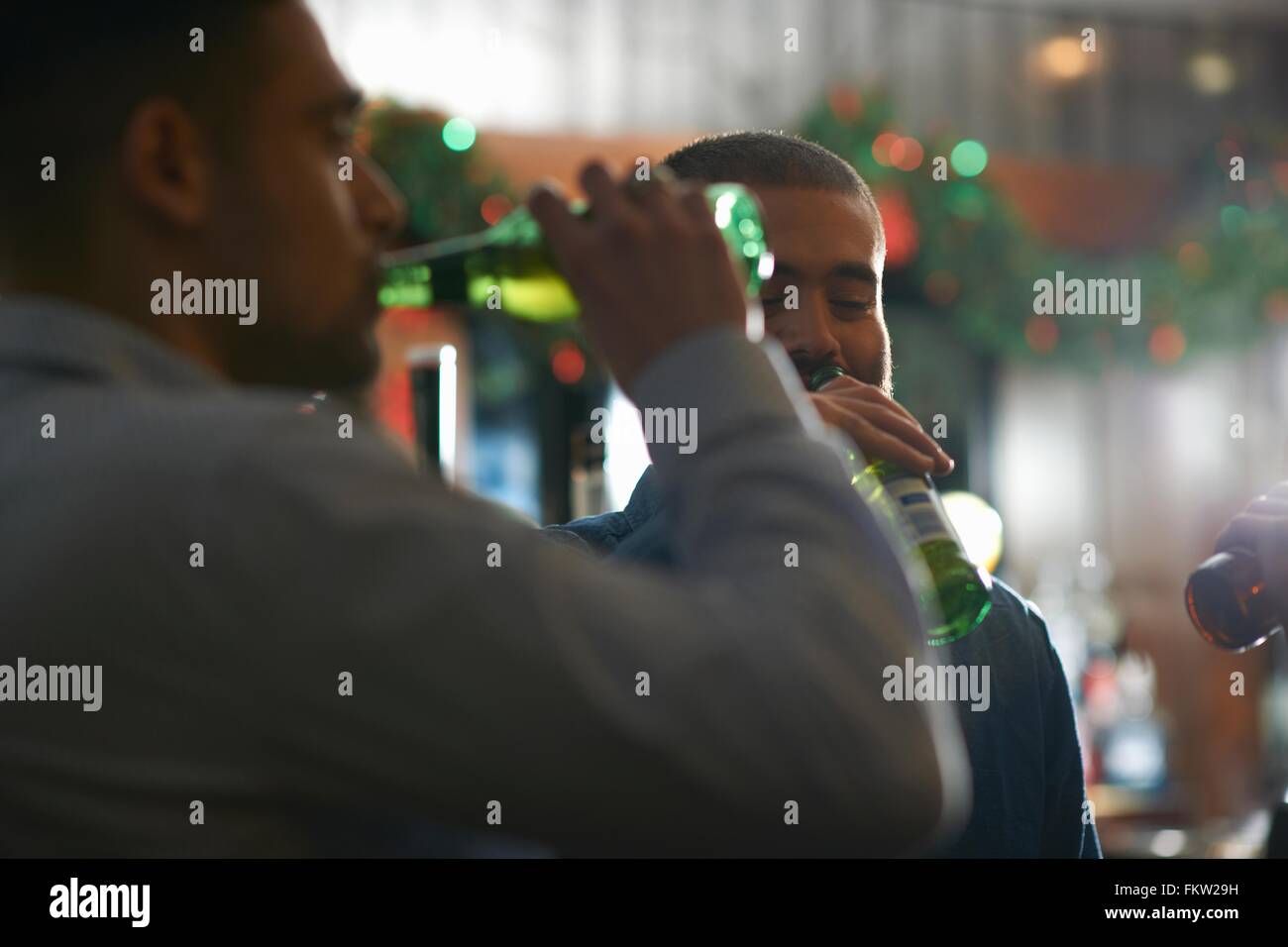 Giovani uomini in public house a bere birra dalle bottiglie Foto Stock