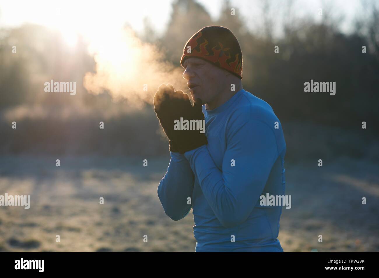 Runner in maglia da indossare guanti e cappello, strofinando le mani insieme, respirando aria fredda Foto Stock