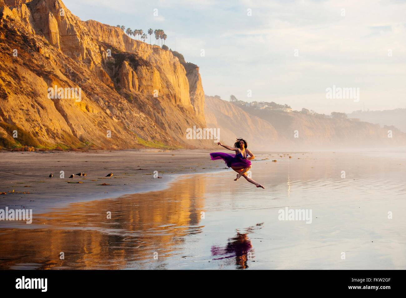 Femmina giovane ballerino, jumping, a metà in aria, acqua oltre a beach, San Diego, California, Stati Uniti d'America Foto Stock