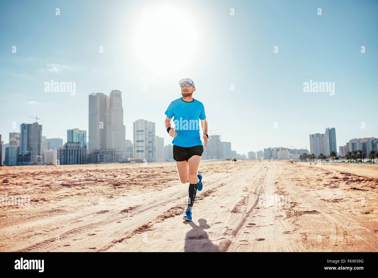 Lunghezza piena vista frontale di metà uomo adulto in esecuzione sulla sabbia da sky i raschiatori, Dubai, Emirati Arabi Uniti Foto Stock