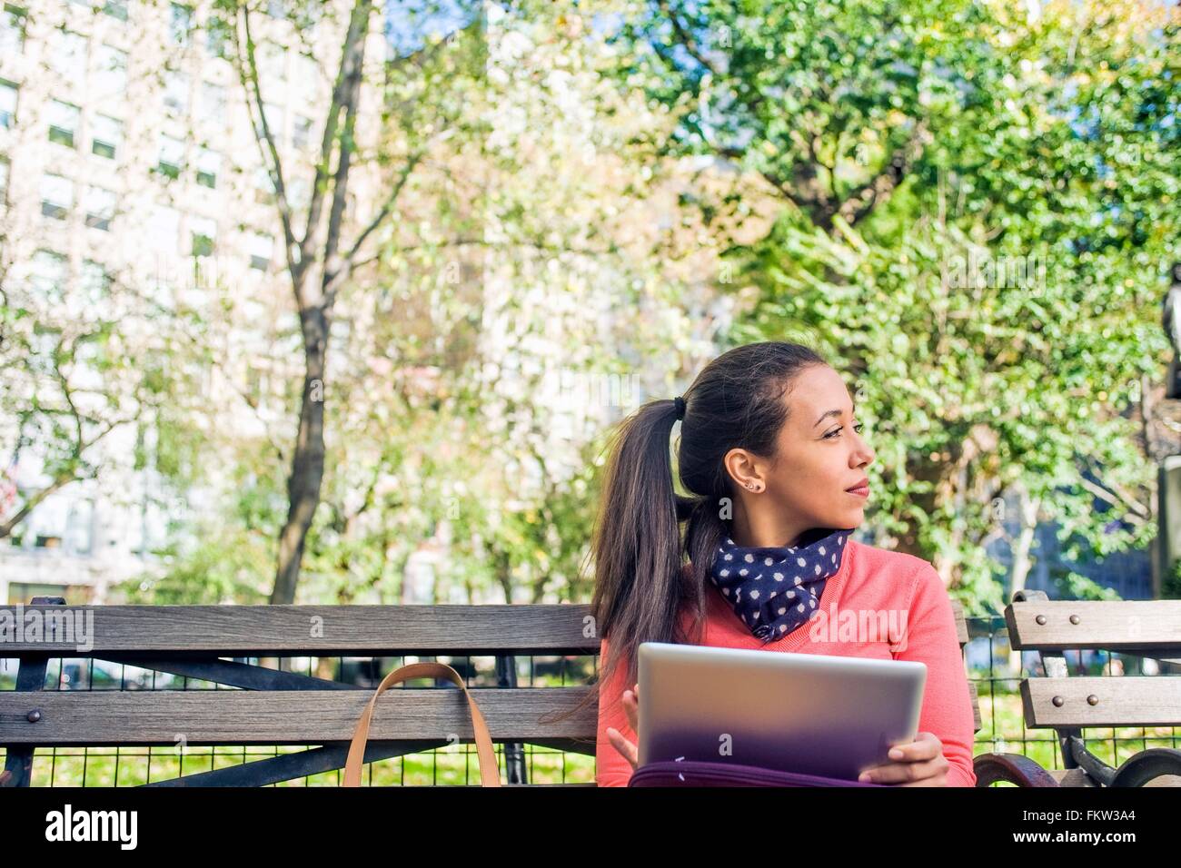 Giovane donna guardando lateralmente da una panchina nel parco mentre usando tavoletta digitale Foto Stock