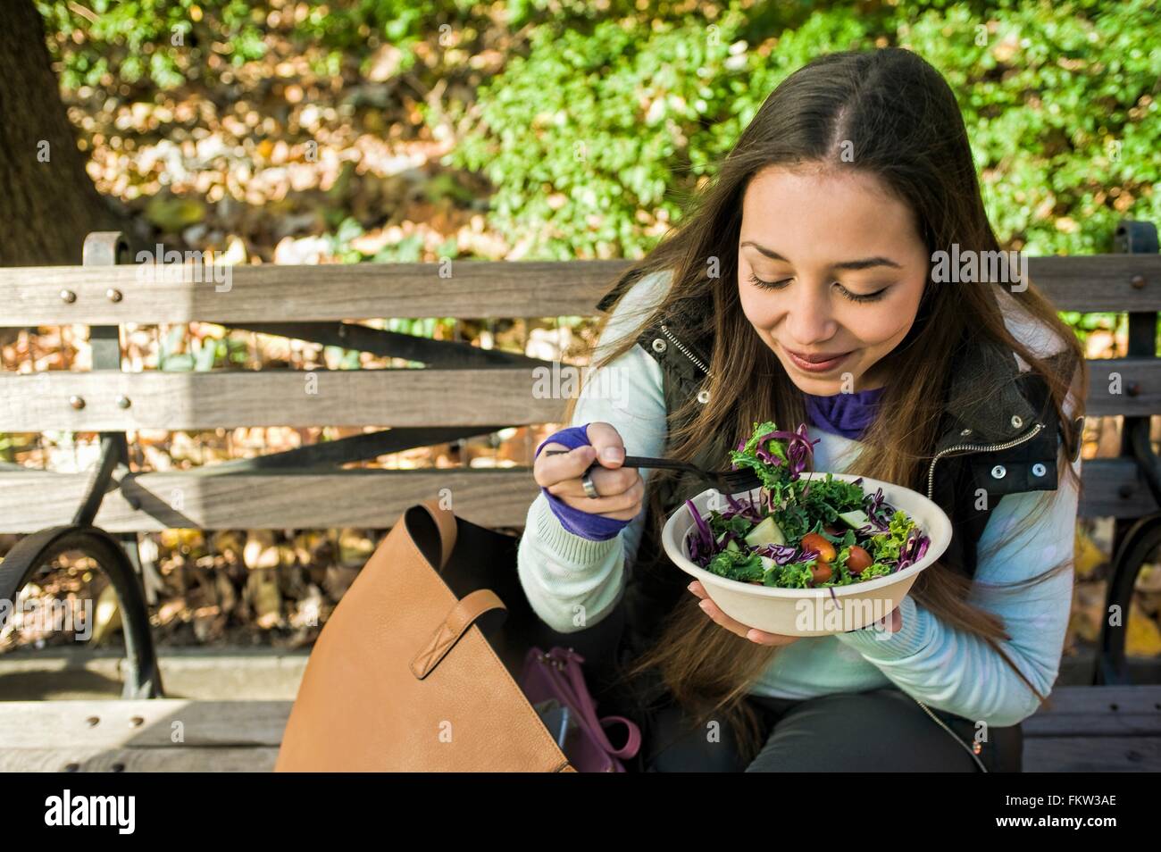 Giovane donna seduta su una panchina nel parco di mangiare insalate a pranzo Foto Stock