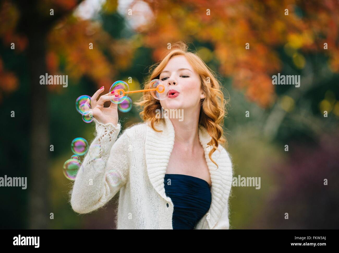 Giovane donna bella con il rosso dei capelli ondulati soffiare bolle nella foresta di autunno Foto Stock