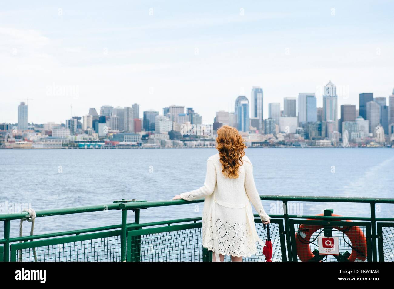 Vista posteriore della donna che guarda la skyline della città dal traghetto passeggero sul Puget Sound, Seattle, Stati Uniti d'America Foto Stock