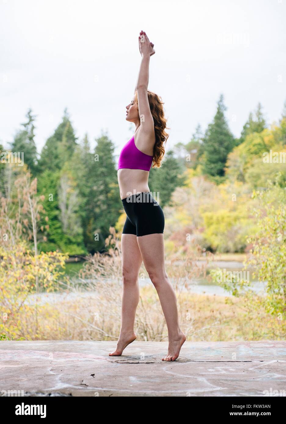 Vista laterale della giovane donna a praticare yoga sul lungolago di foresta Foto Stock