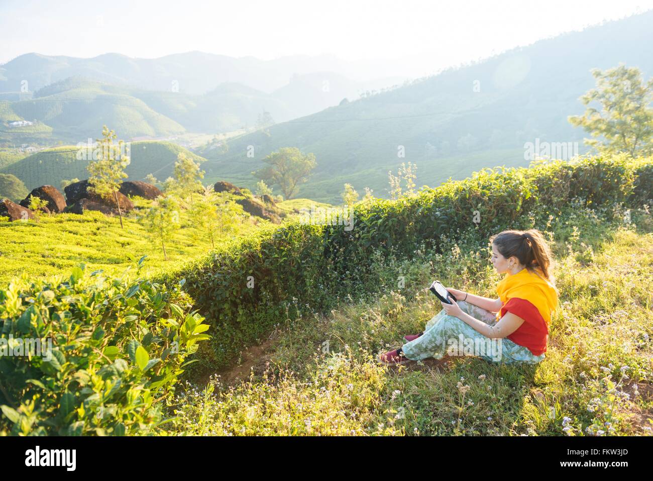 Giovane donna lettura digitale compressa a piantagioni di tè vicino a Munnar Kerala, India Foto Stock