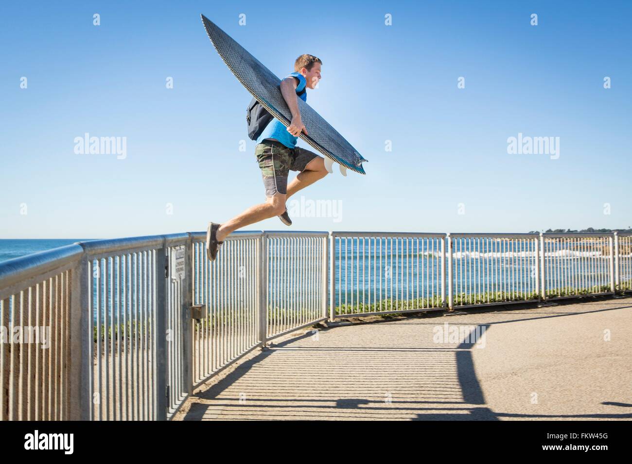 Giovane uomo, portando le tavole da surf, saltando da ringhiere accanto al mare Foto Stock