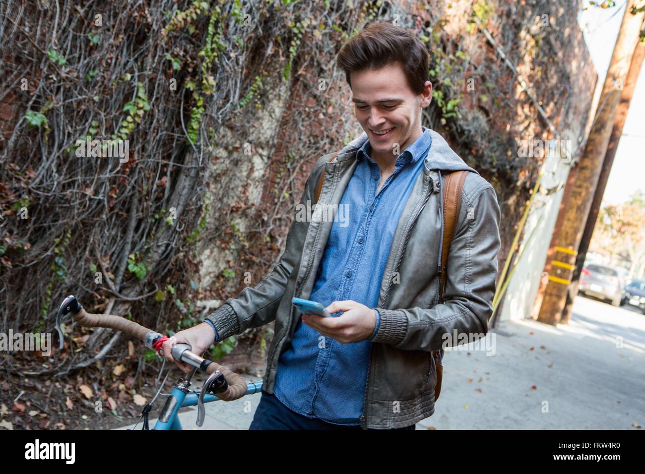 Giovane uomo passeggiando con ciclo sul marciapiede la lettura di testi dello smartphone Foto Stock