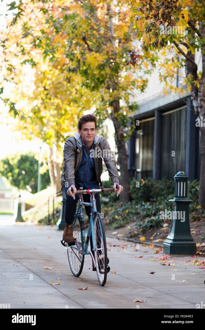 Giovane uomo in bicicletta lungo il marciapiede Foto Stock