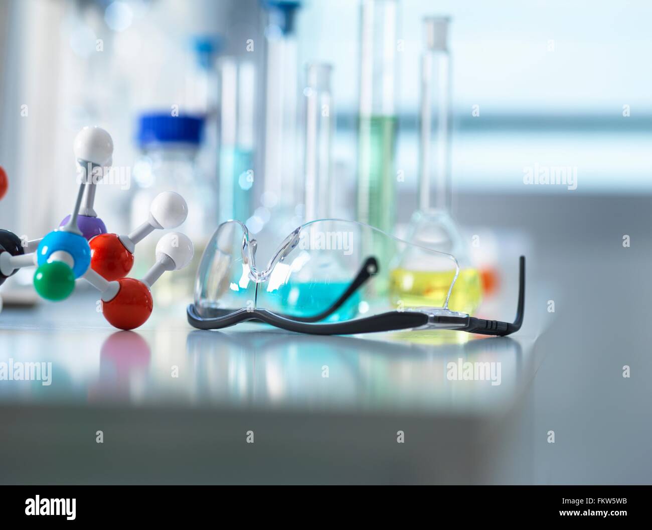 Occhiali di sicurezza e modello molecolare sul banco da laboratorio, apparecchiature scientifiche in background Foto Stock