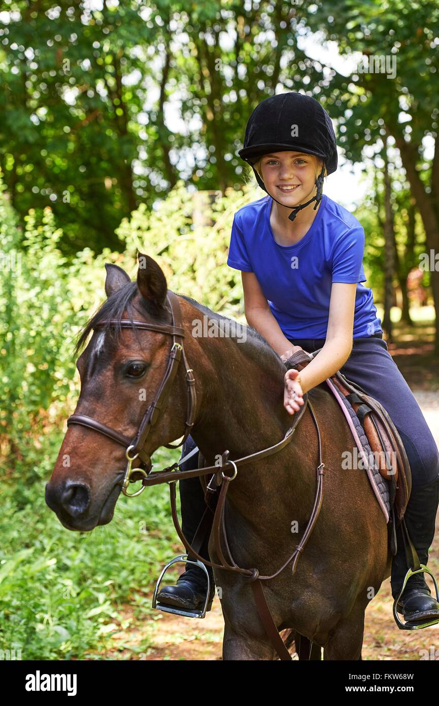 Ragazza sul cavallo che indossa riding hat guardando sorridente della fotocamera Foto Stock