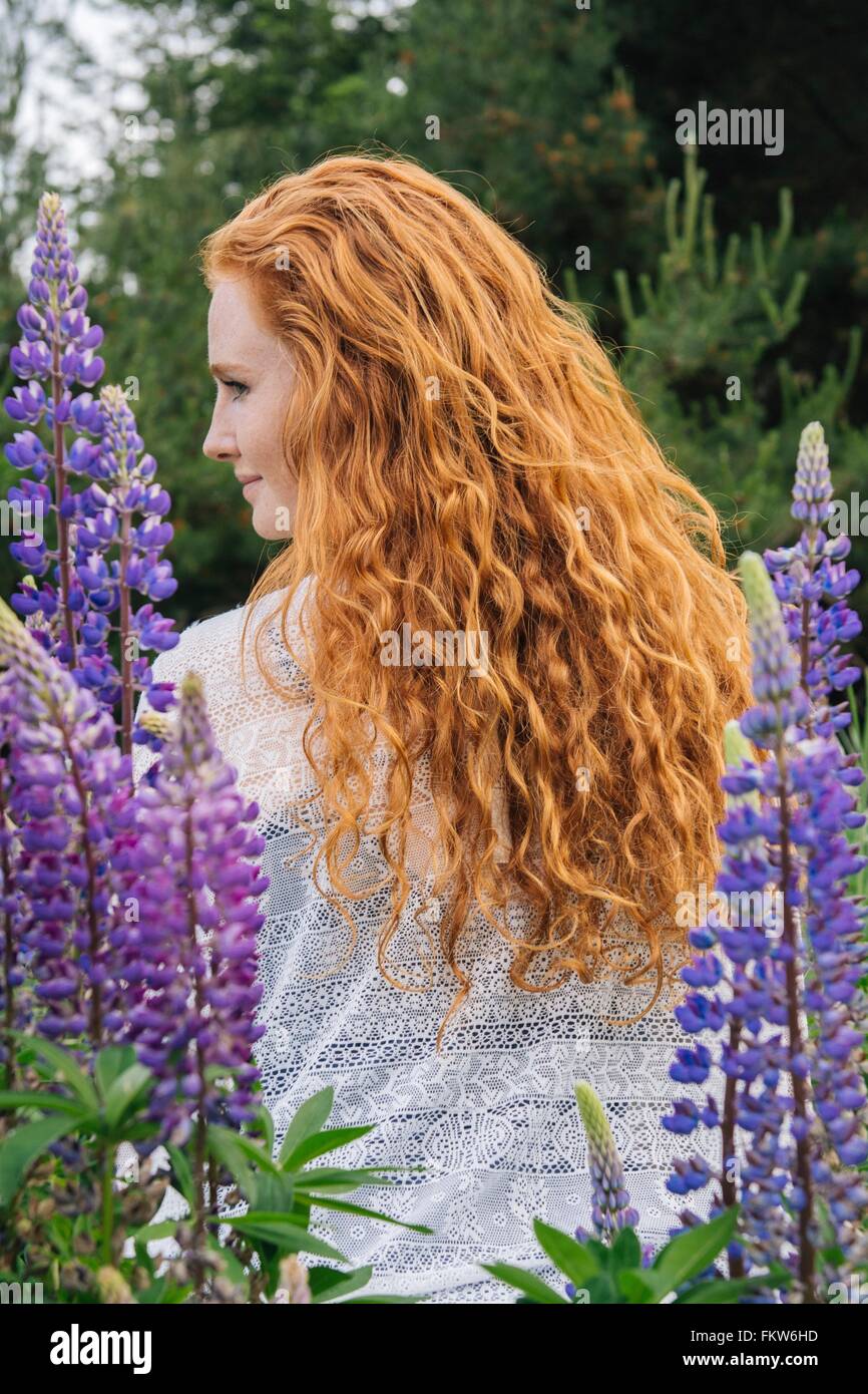Vista posteriore del Ritratto di giovane donna con lunghi capelli rossi tra fiori selvatici viola Foto Stock