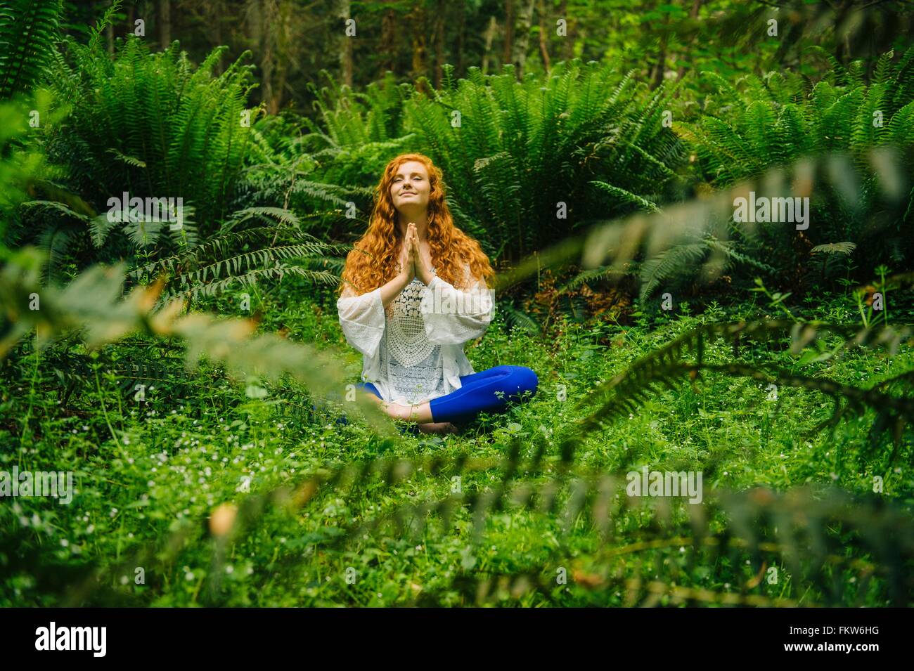 Giovane donna a praticare yoga nella posizione del loto in foresta Foto Stock
