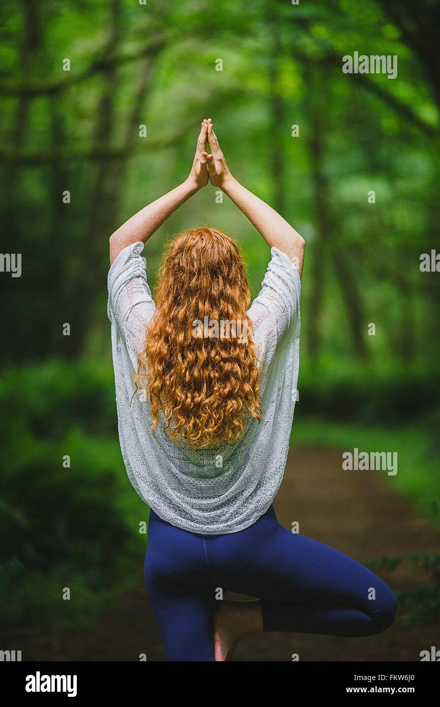 Vista posteriore della giovane donna nella foresta a praticare yoga in posa ad albero Foto Stock