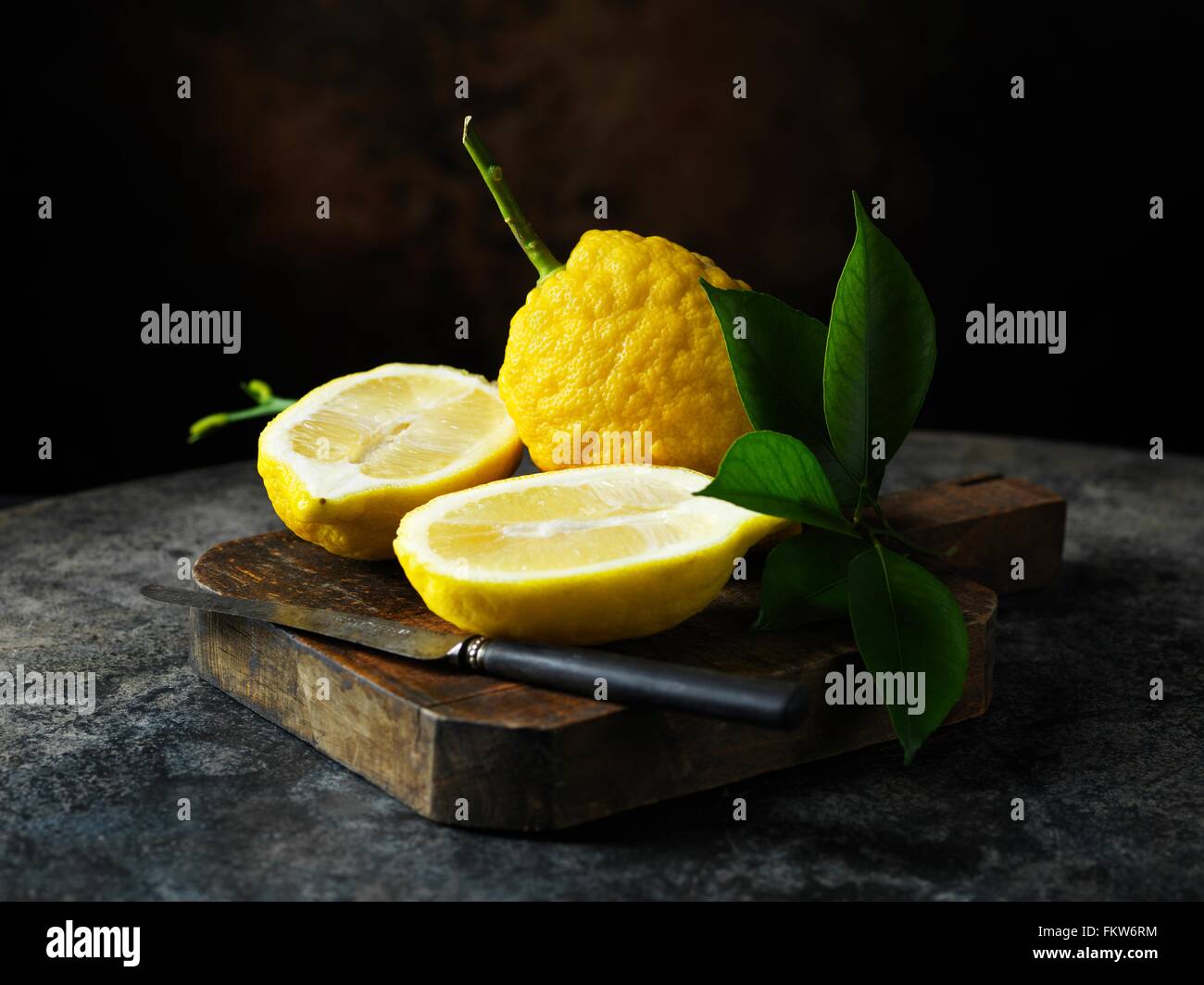 Textured limone intero e dimezzato con foglie sul tagliere di legno con coltello vintage Foto Stock