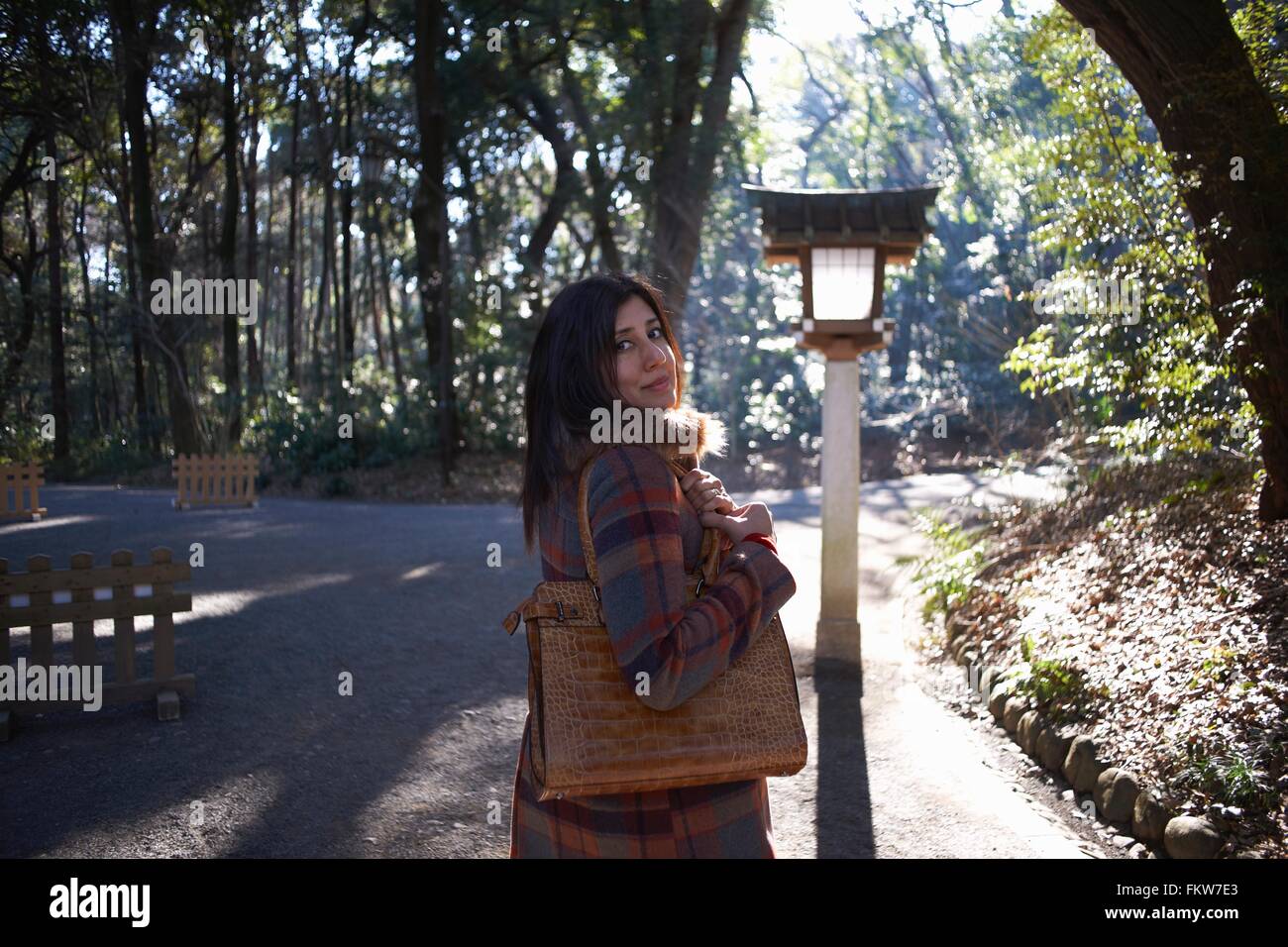 Ritratto di femmina matura tourist guardando sopra la sua spalla in park, Tokyo, Giappone Foto Stock