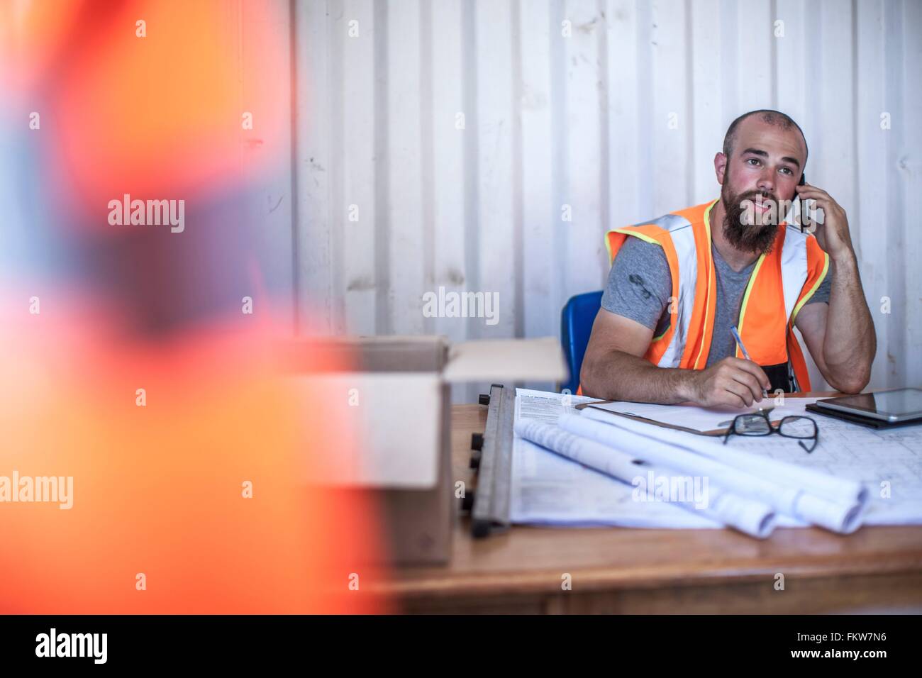 Costruzione lavoratore seduto alla scrivania parlando sullo smartphone in cabina portatile Foto Stock