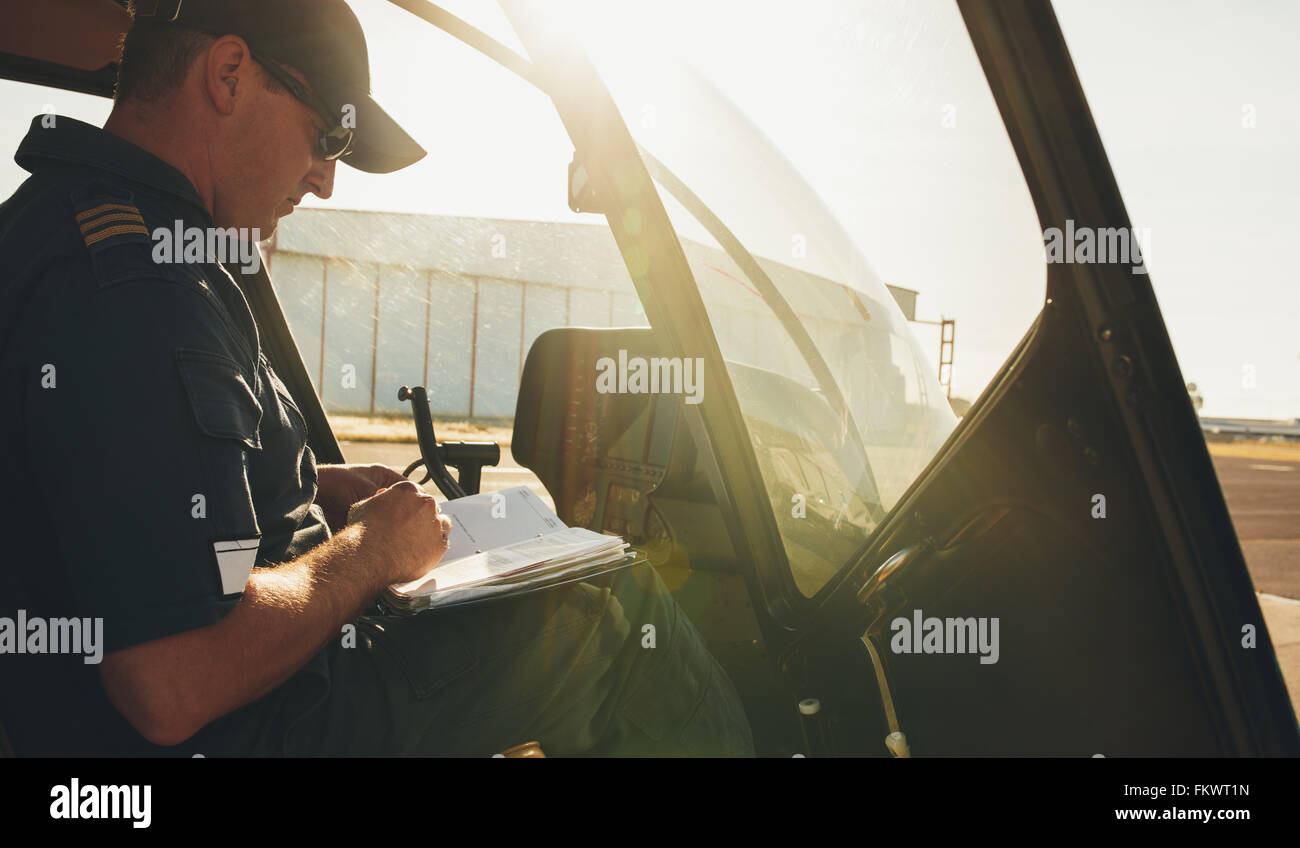 Elicottero di controllo pilota il manuale di volo prima di un decollo. L'elicottero è a terra con la luce del sole. Foto Stock