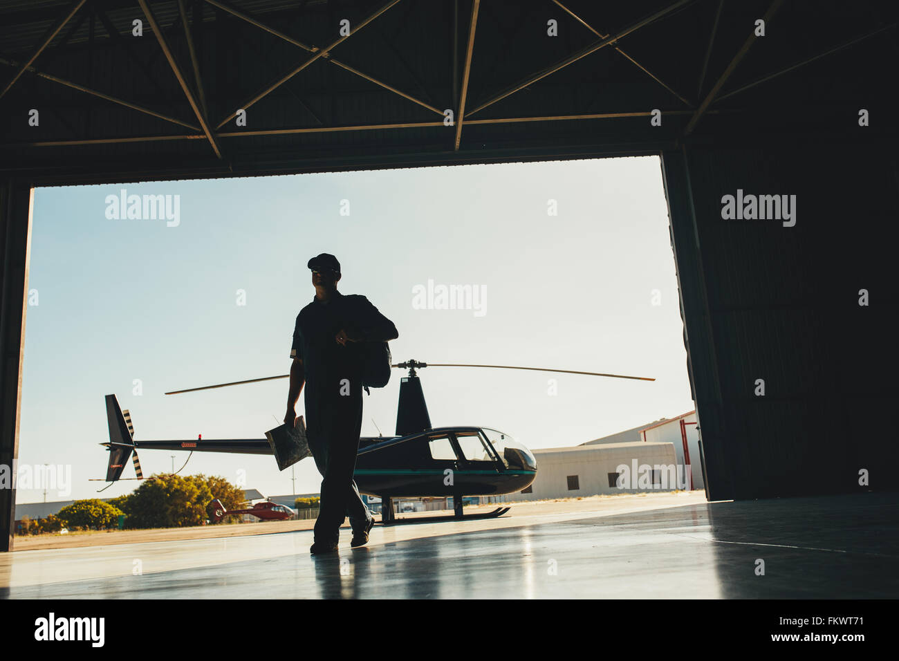 Silhouette di un pilota che arrivano all'aeroporto con un elicottero in background. Pilota di elicottero in hangar aereo. Foto Stock