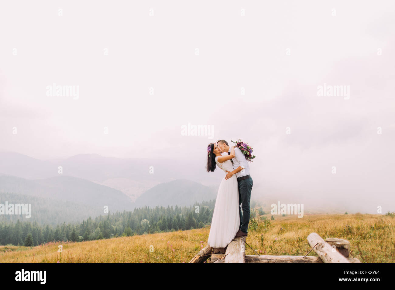 Bella sposi bacio sul ponte di legno. Nebbioso giorno in montagna Foto Stock