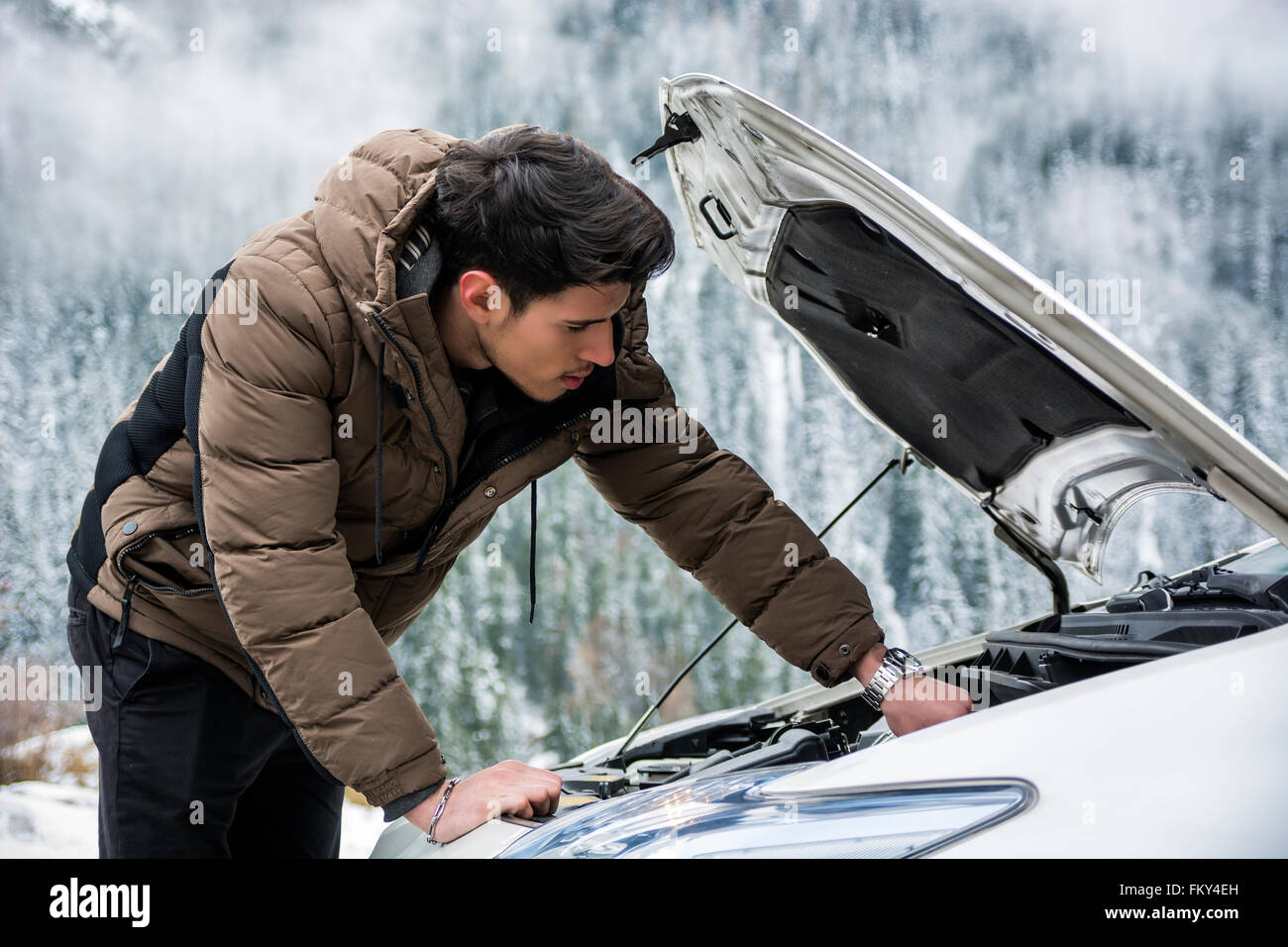 Giovane uomo vicino auto con aprire il cofano motore di ispezione. Boschi innevati sullo sfondo Foto Stock