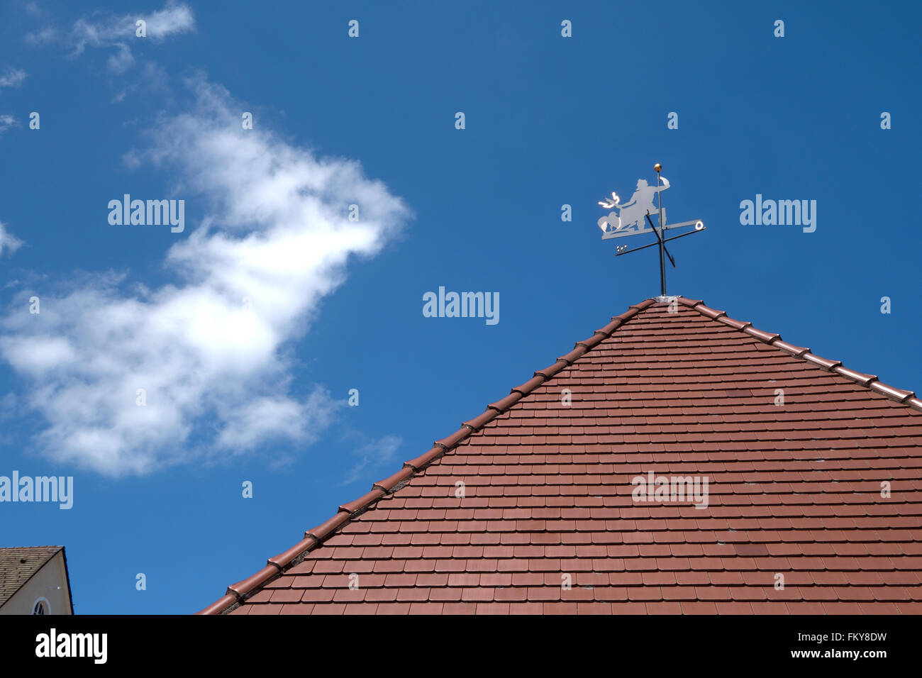 Banderuola con il diavolo e indicatore di direzioni di bussola su un tetto a punta con tegole rosse contro un cielo blu. Foto Stock