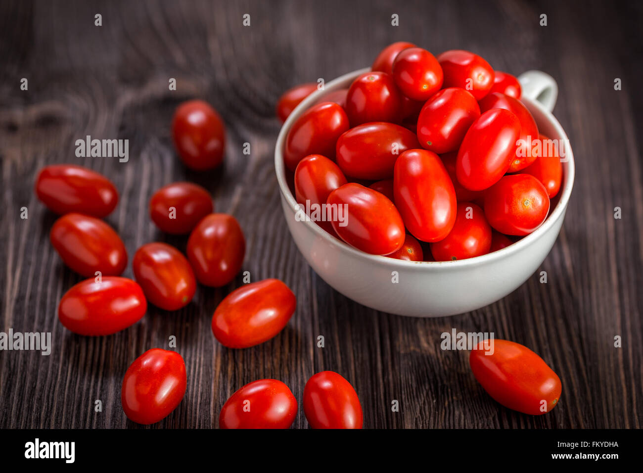 Una tazza di pomodori ciliegia al buio su un sfondo di legno Foto Stock