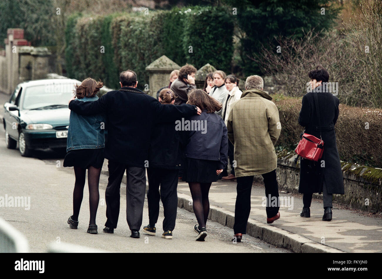 Un gruppo di adulti e di bambini che abbracciano esternamente Dunblane scuola primaria, Scozia, poco dopo l'incidente di tiro nei locali. Il Dunblane School Massacre è stato uno dei più letali omicidi di massa nella storia del Regno Unito, quando pistolero Thomas Hamilton ucciso sedici bambini e un insegnante a Dunblane scuola primaria vicino a Stirling, in Scozia il 13 marzo 1996, prima di uccidere se stesso. Come un risultato di uccisioni, due nuove armi da fuoco gli atti sono passati, che rese effettivamente la proprietà privata di pistole illegale in Gran Bretagna. Foto Stock