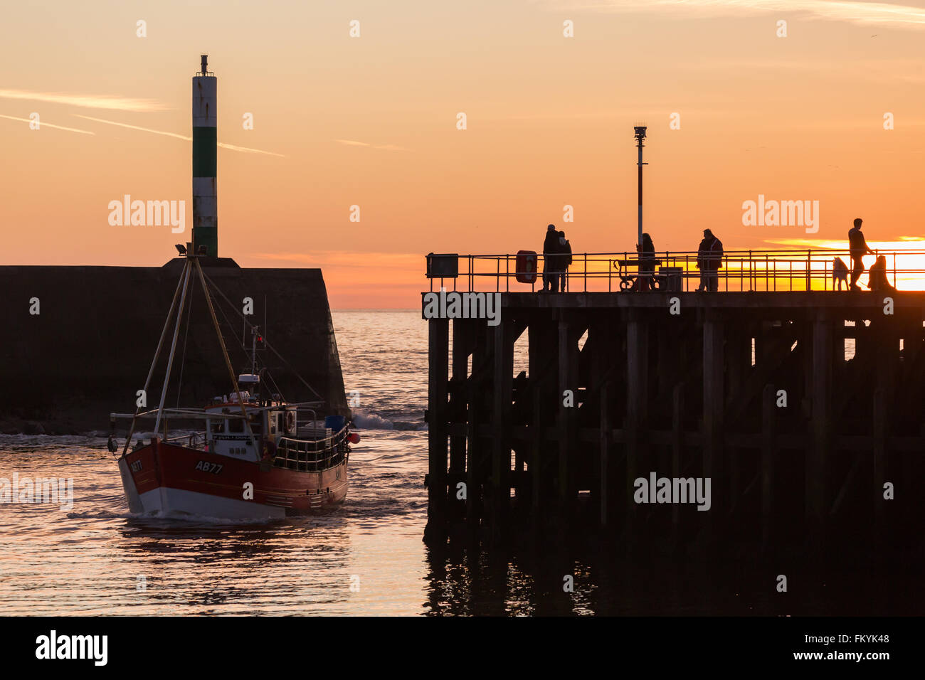 Persone Godetevi il tramonto dal pontile in legno come i pescatori locali entra in porto nella cittadina balneare di Aberystwyth, che si trova sulla costa occidentale del Galles, UK. Credito: Ian Jones/Alamy Live News Foto Stock