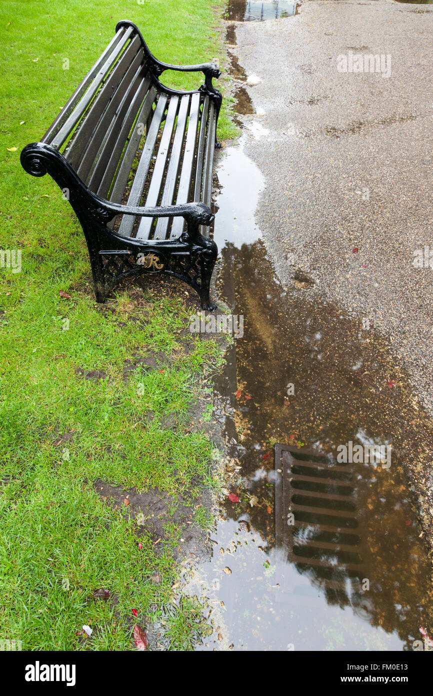 Scarico ostruito e una pozza di acqua piovana accanto a un banco in un parco, Nottinghamshire, England, Regno Unito Foto Stock