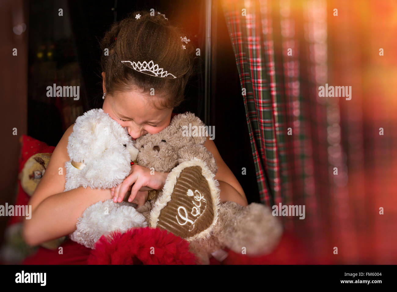 Sorridente adorabile bambina vestito in un lussureggiante abito rosso, molto abbraccia due orsi di peluche, cuore con iscrizione amore Foto Stock