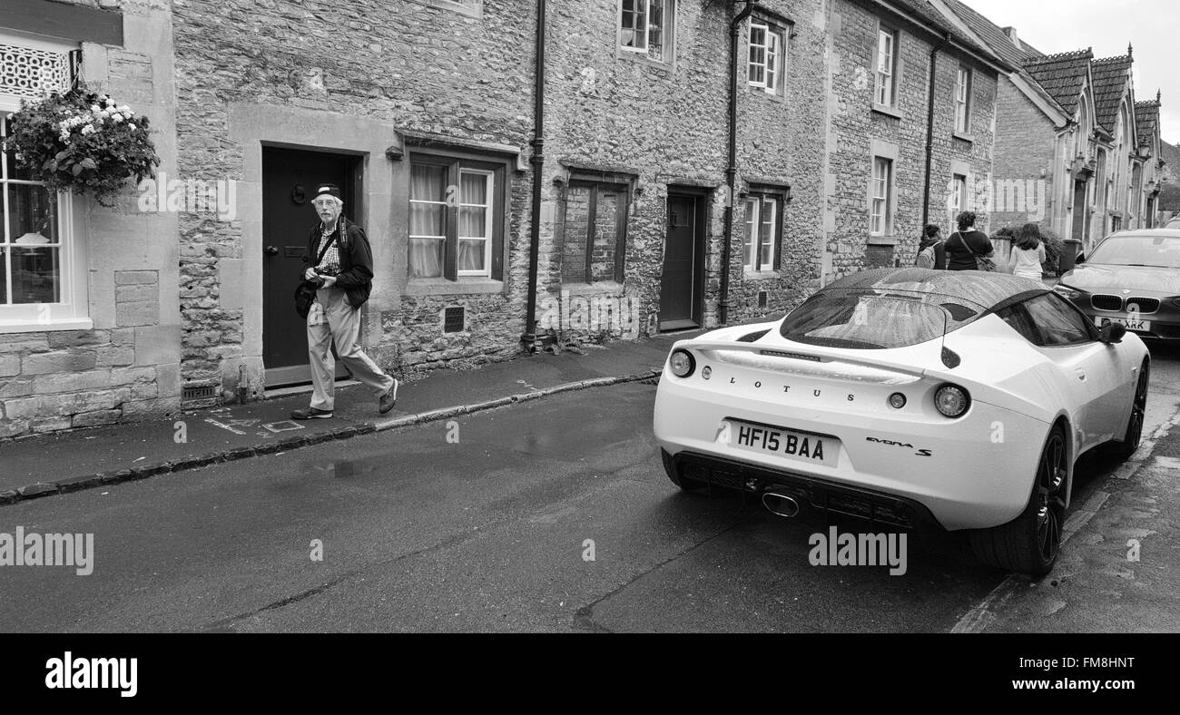 Nuova Lotus auto nel vecchio e pittoresco villaggio inglese di avebury con anziani fotografo passato a piedi sotto la pioggia di avebury REGNO UNITO Foto Stock