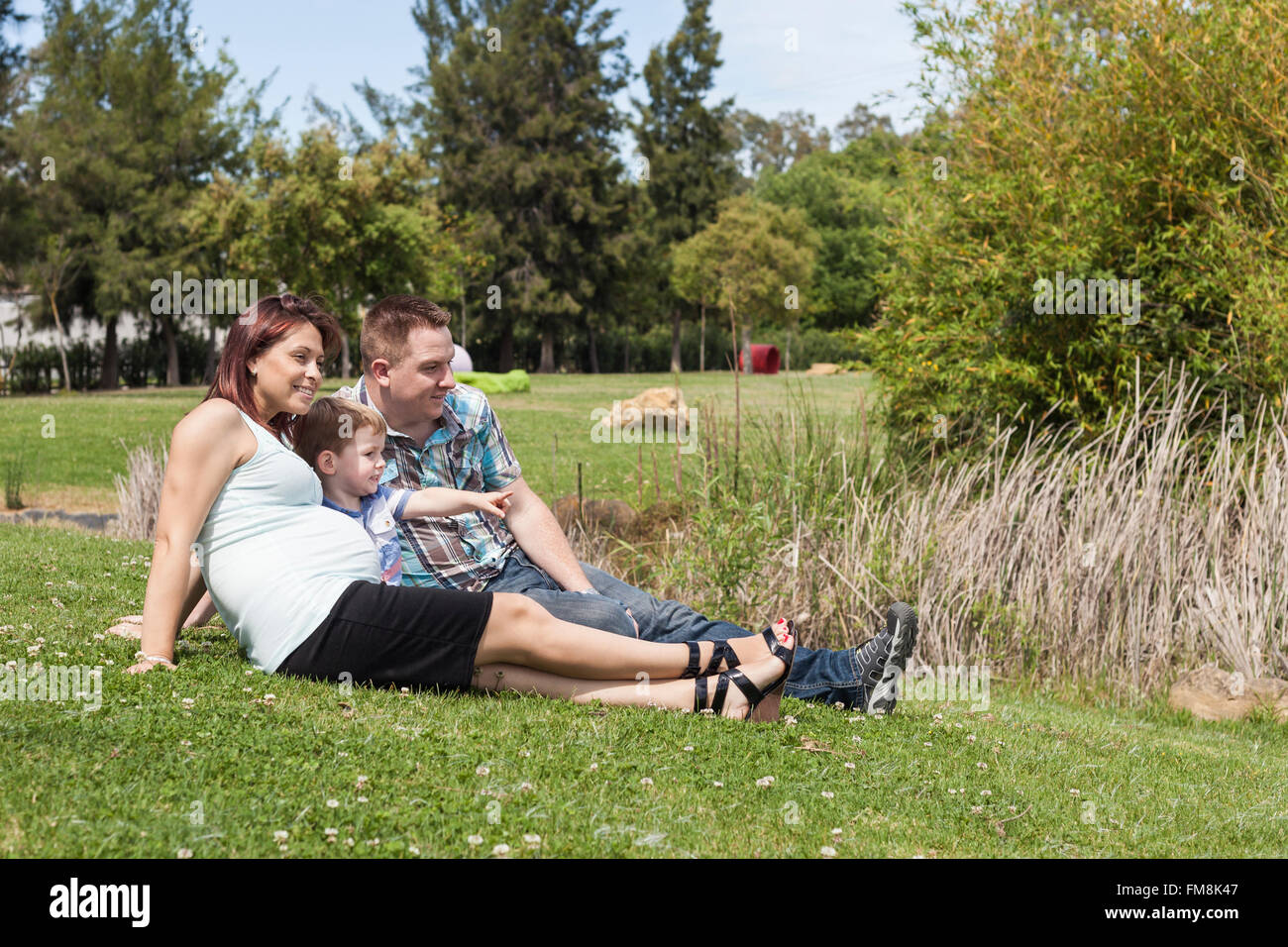 Giovani felice famiglia gravidanza rilassante nel parco e godersi la giornata estiva all'aperto. Foto Stock